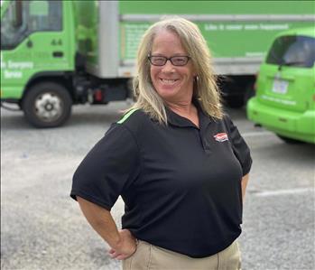 SERVPRO female employee smiling in front of green trucks