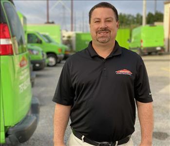 SERVPRO male employee standing in front of green trucks